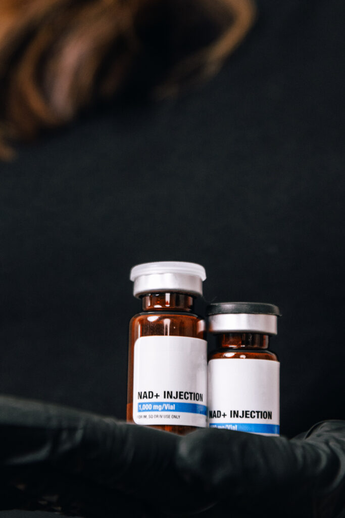Glass vials of NAD are shown in the center of the image against a black background. These vials are used to hold the NAD+ used in NAD+ injections in Lenexa.